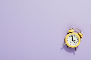 A vibrant yellow alarm clock on a purple surface with ample copy space, perfect for design projects.